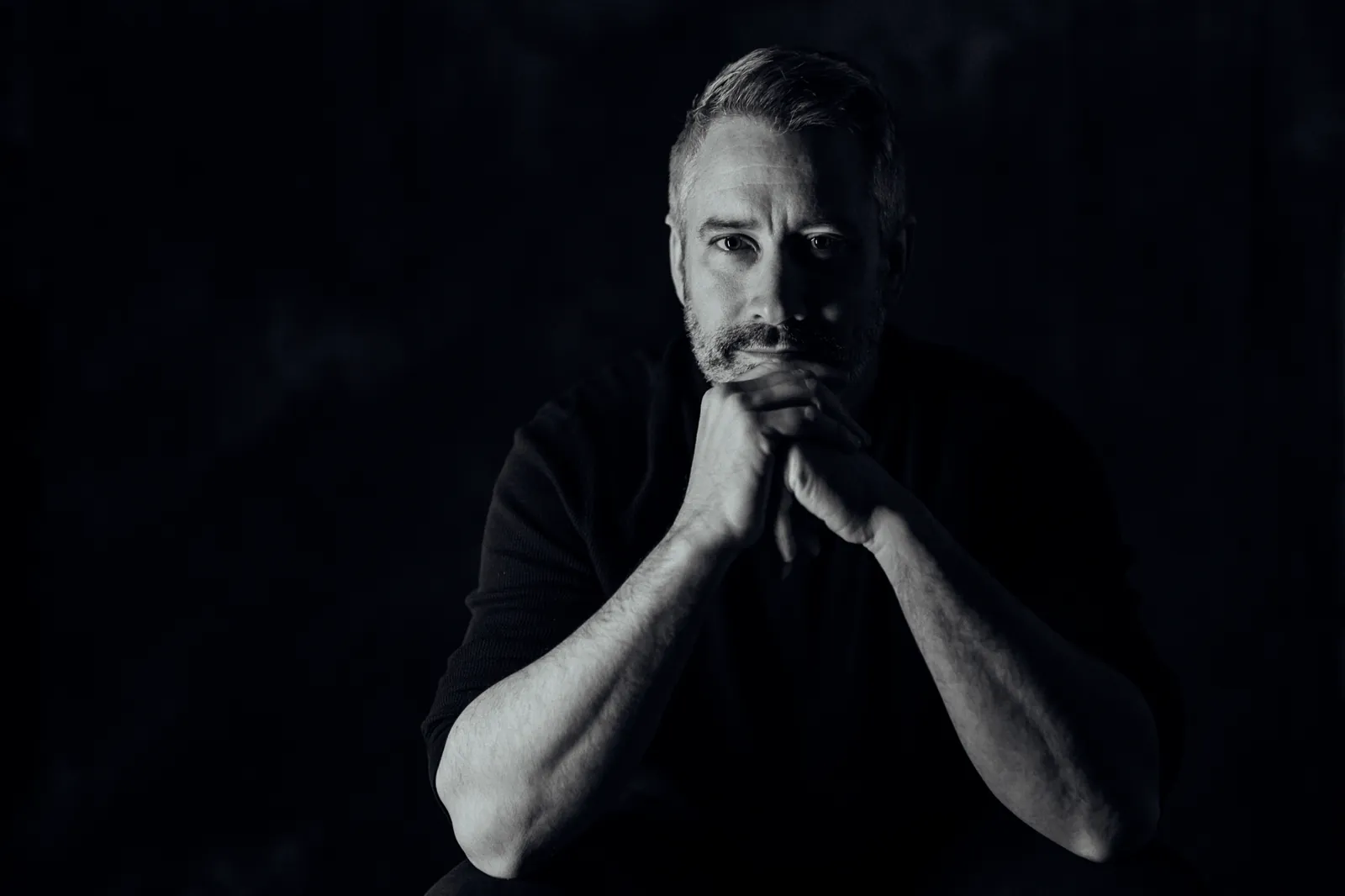 Black and white portrait of Matt MacIsaac, hands clasped under his chin